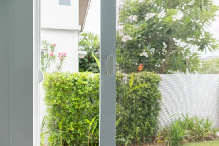 Closeup of an open screen door, leading to a backyard.